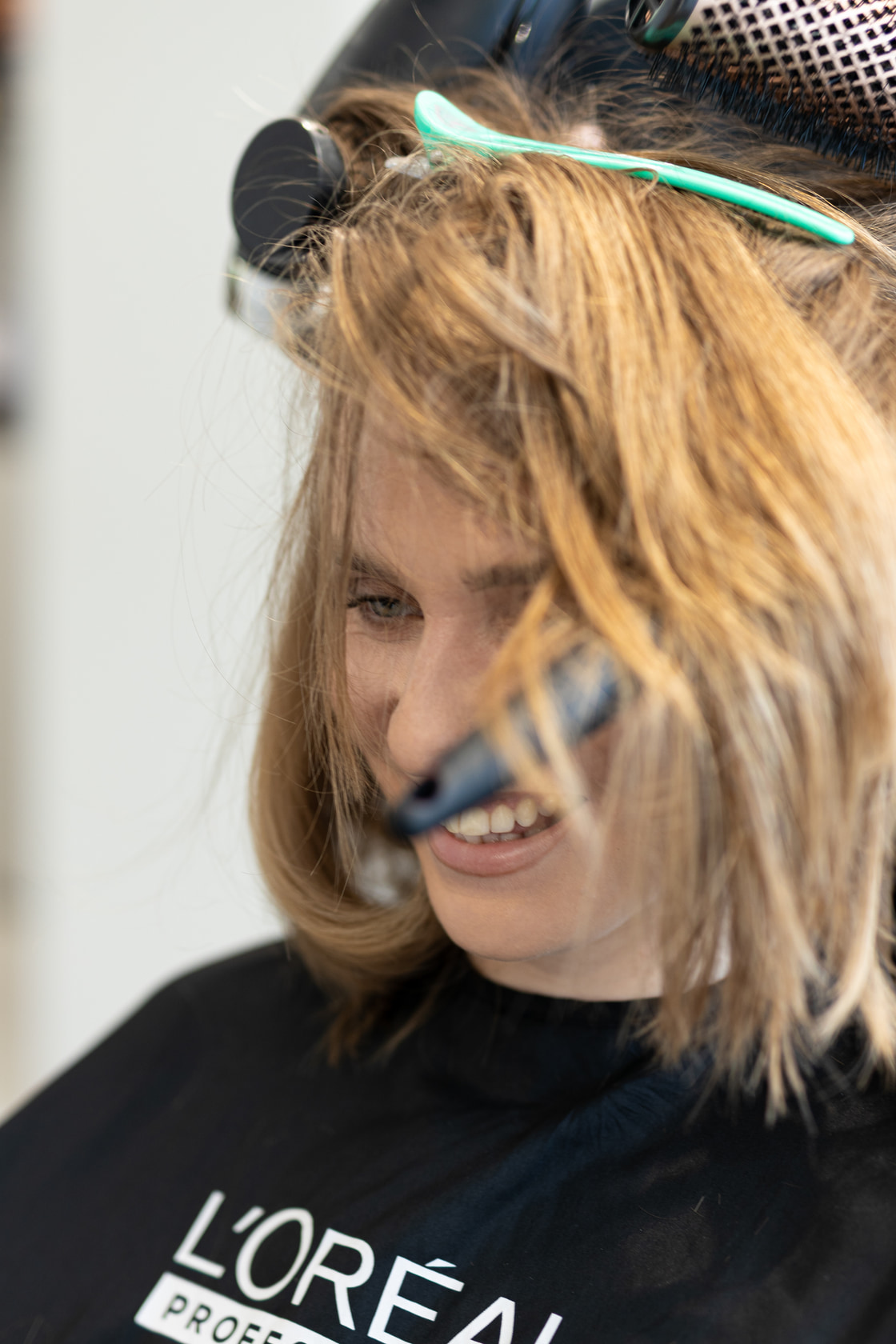 Cliente souriante pendant le brushing, cheveux soulevés par la brosse ronde