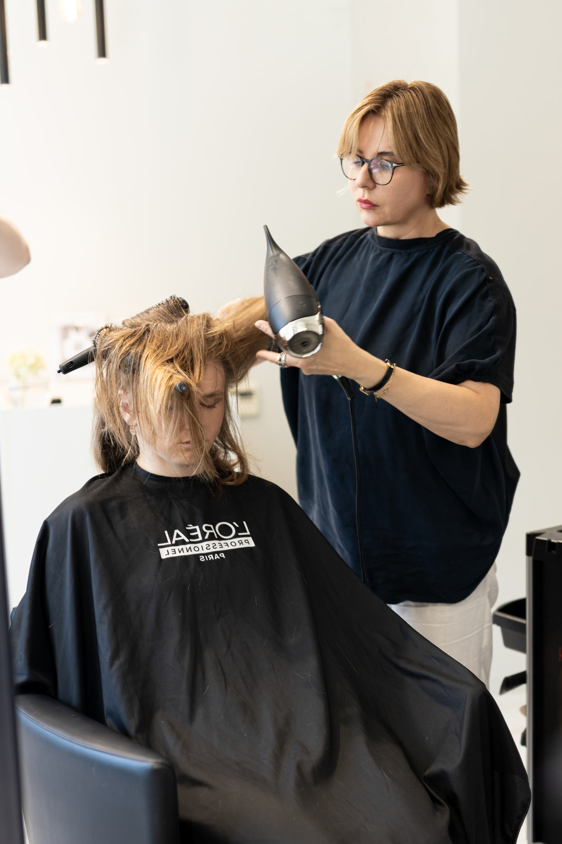 Coiffeuse réalisant un brushing derrière le fauteuil