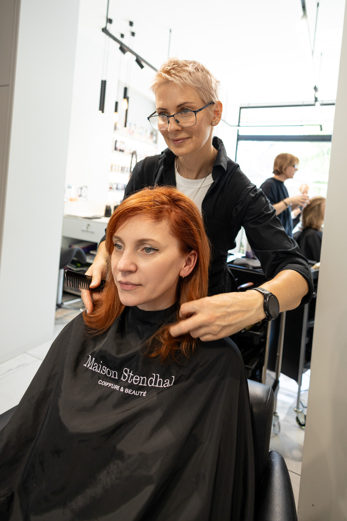 Coiffeuse derrière une cliente aux cheveux fraîchement colorés en roux